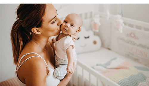 Woman kissing baby on cheek while holding it in nursery room