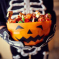 Child in costume holding jack-o'-lantern bucket full of Halloween candy