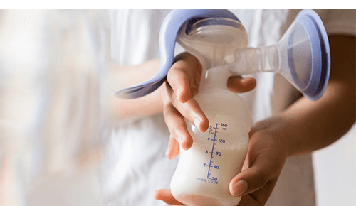 Person holding breast pump attached to bottle filled with milk