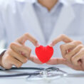 Doctor holding red heart with stethoscope on desk in front of them