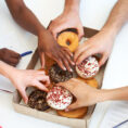 Many hands reaching for donuts from a box in the middle of the table