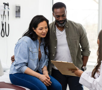 Couple talking with a doctor who is showing them a clipboard with information