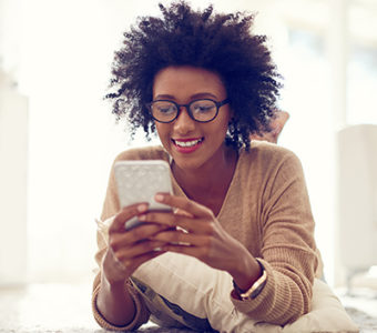 Woman laying on the floor looking at her phone while smiling