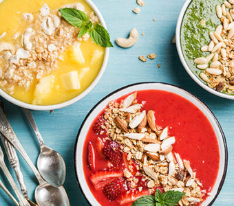 Bowls of different fruit smoothies topped with nuts and fruit