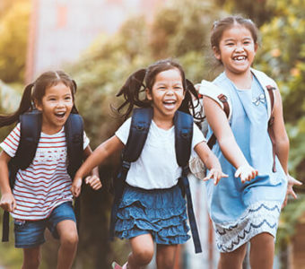 Children holding hands and wearing backpacks on their way home from school