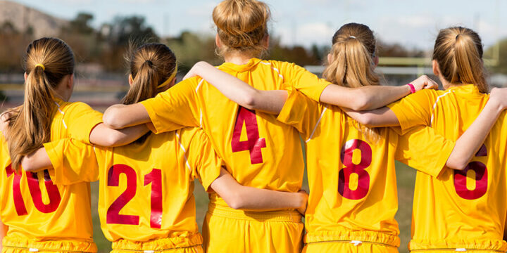 Back of group of teenagers hugging each other and wearing sports uniforms