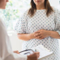 Woman with hands over stomach talking to doctor in a doctor's office