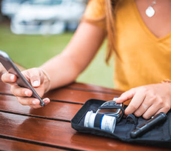 Diabetic person measuring blood sugar levels and looking at phone