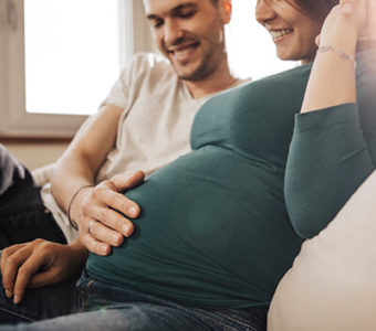 Couple smiling while man holds his hand on the woman's pregnant stomach