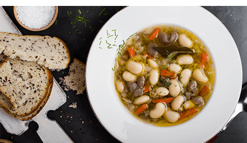 bowl of Cabbage and White Bean Soup with Sausage with bread on the side