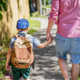 Parent and child with backpack holding hands while walking down a sidewalk together