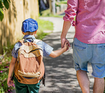 Parent and child with backpack holding hands while walking down a sidewalk together