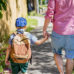 Parent and child with backpack holding hands while walking down a sidewalk together