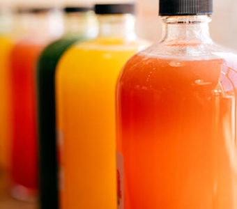 Glass bottles lined up in row and filled with different types of pressed juices