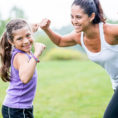 Mother and daughter smiling and flexing their arm muscles outdoors