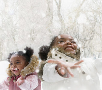 Two children smiling with arms out looking up at the snowflakes falling