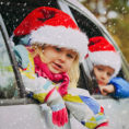 Children wearing Santa hats looking out the windows of a car