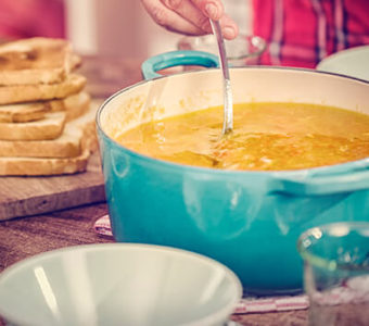 Person stirring a large pot of soup with grilled cheese sandwiches sitting next to it on the counter