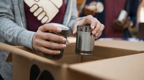 Closeup of person putting metal food cans in cardboard box