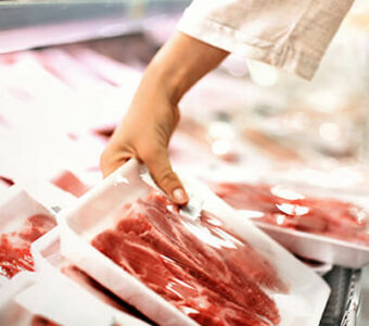 Person picking up a package of red meat from a grocery store display