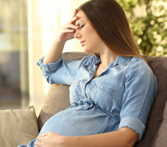 Pregnant person holding head and frowning