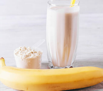 Blender cup with a protein shake sitting next to a measuring cup of protein powder and a banana