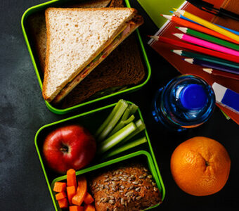 Several lunchbox containers with a variety of healthy food and snacks sitting on top of a chalkboard