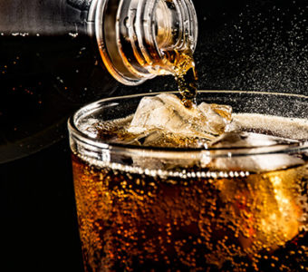 Soft drink being poured from bottle into glass filled with ice