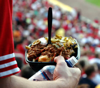 Closeup of person standing in packed sports stadium holding a plate of loaded nachos