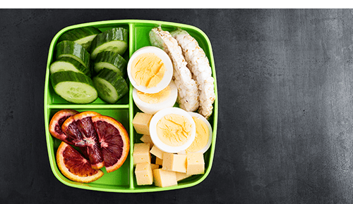 Lunchbox container with sliced fruit and vegetables, cheese and boiled egg slices