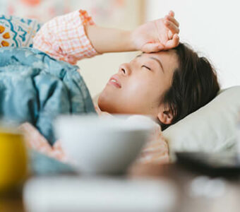 Sick person lying in bed with hand to forehead