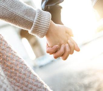 Closeup of two people holding hands while walking down the street