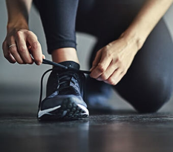 Closeup of someone kneeling on the ground to tie the laces of their athletic shoe