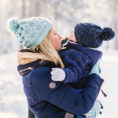 Mother holding baby, both wearing cold weather gear, in winter outside