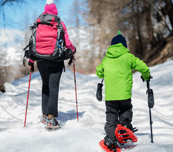 Adult and child walking on snow covered path wearing snow shoes