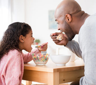 Father and child eating cereal together at kitchen table