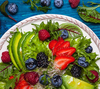 Plate of salad topped with avocado and mixed berries