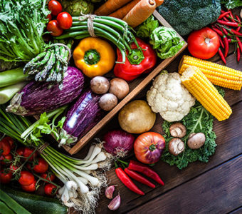 Variety of vegetables around a basket on a wooden background