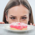 Woman looking longingly at a sprinkle donut sitting on a plate