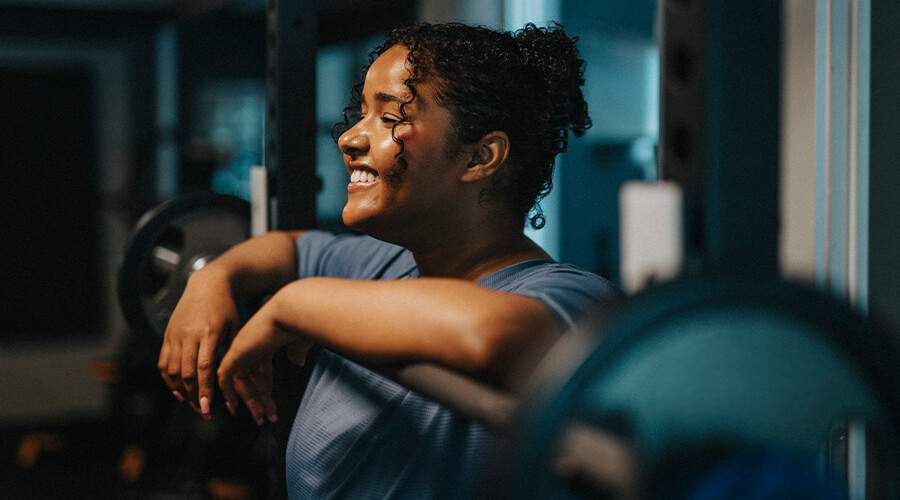 Smiling person leaning on weight lifting machine in gym