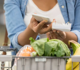 Closeup of person using a smart phone while pushing a grocery store shopping cart with food in it