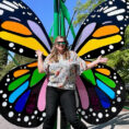 Smiling person in sunglasses in front of butterfly sculpture