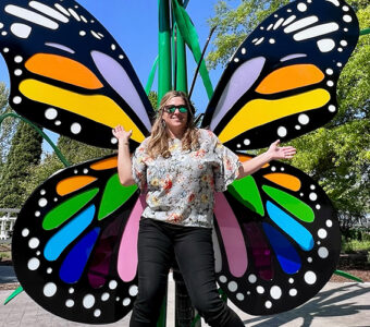 Smiling person in sunglasses in front of butterfly sculpture