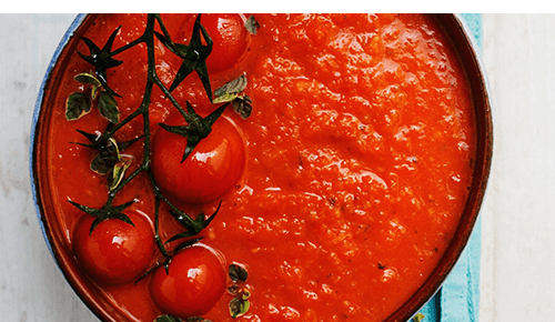 Pot of tomato sauce with whole fresh tomatoes sitting on top