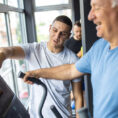 Person using exercise machine with help from a fitness professional