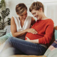 Pregnant person next to partner who has their hand on their stomach