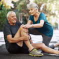 Woman helping injured man sitting on ground, holding knee in pain