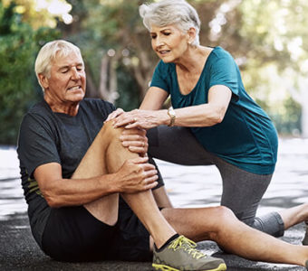 Woman helping injured man sitting on ground, holding knee in pain