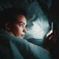 Person in bed lying awake and looking at phone