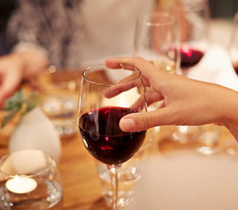 Closeup of a group of people holding wine glasses full of red wine around a dinner table